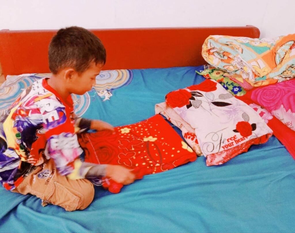 An 8-year-old boy folding a red blanket while making his bed in the morning.