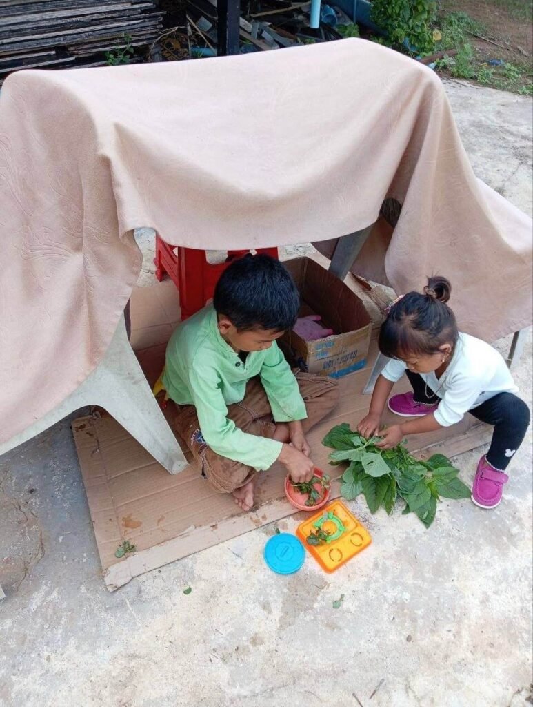 Brother and sister playing underneath a homemade tent made from chairs and a blanket.