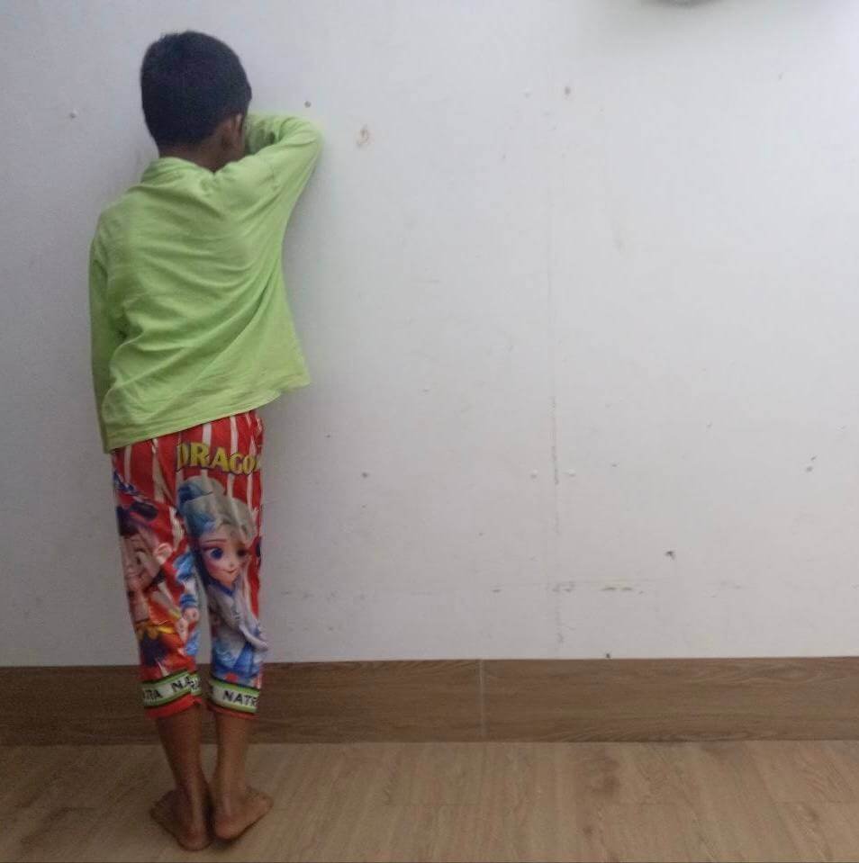 A young boy standing facing a white wall, closing his eyes to count while playing hide and seek.