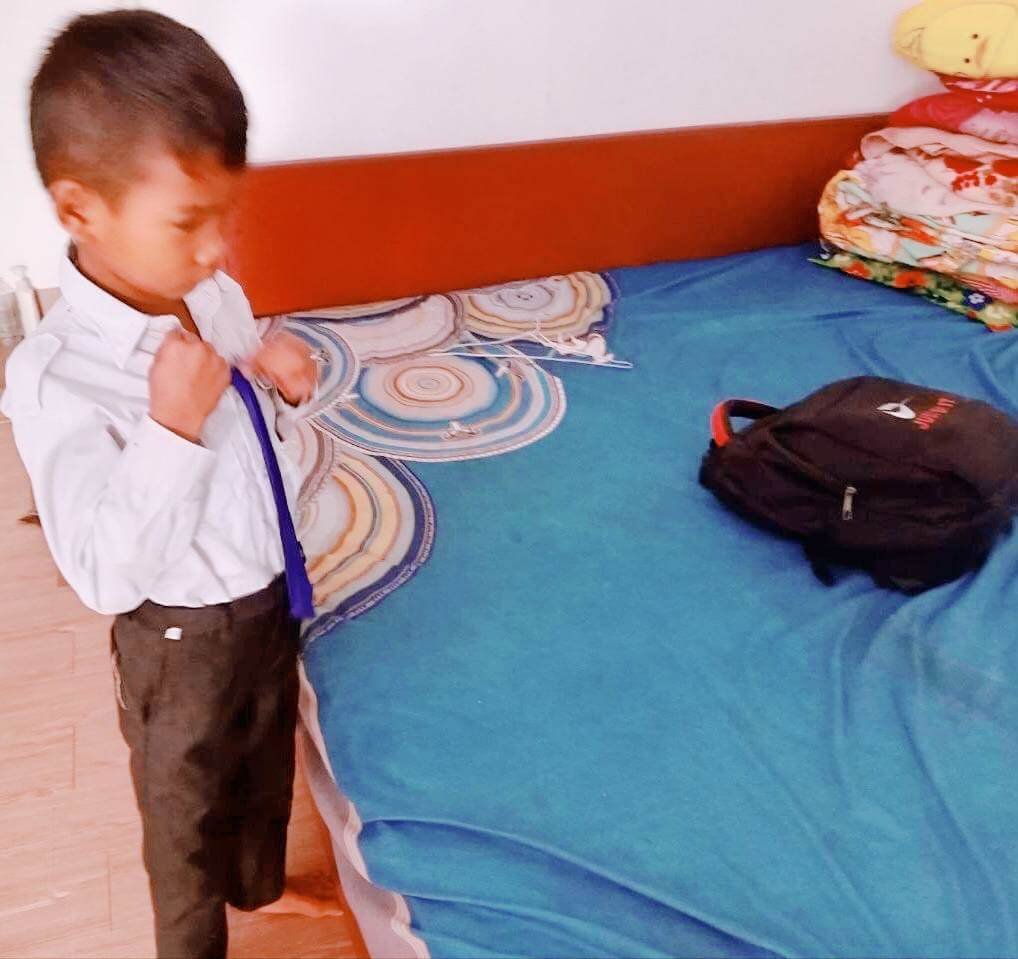 A young boy carefully adjusting his blue tie while dressing for school.
