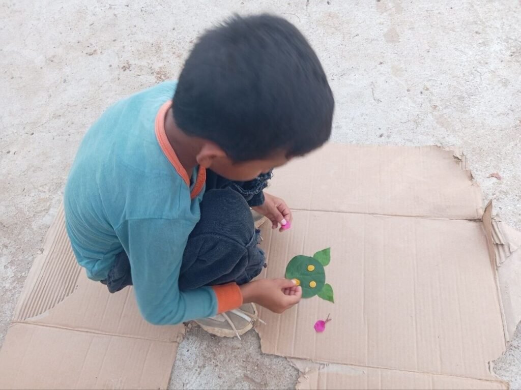 A child finishing a leaf cat craft by placing a pink flower petal to look like a bow on one of the green leaf ears.