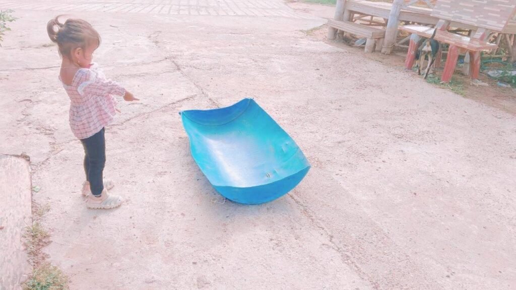 A young girl pointing at a blue plastic barrel that has been cut in half to be used as a backyard toy.
