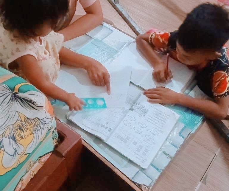 A mother helping her young son and toddler daughter practice writing and drawing in their workbooks.