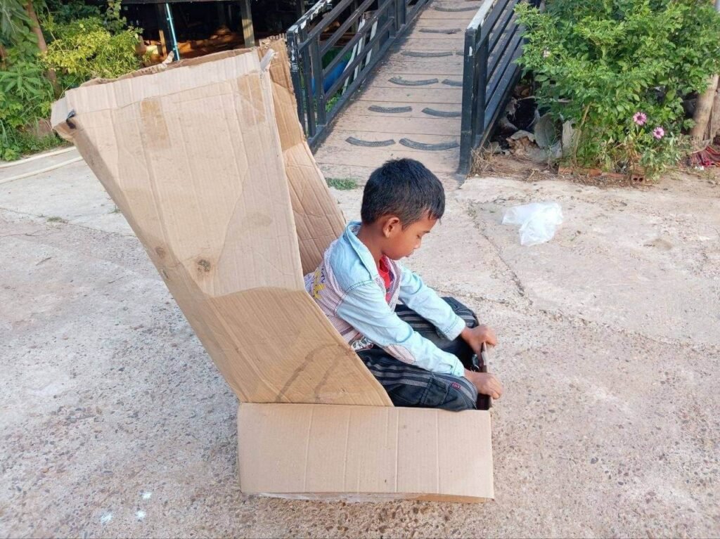 A young boy sitting inside a large DIY cardboard box shaped like a car with a tall canopy.