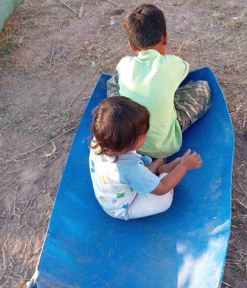 Two children sitting inside a large blue halved plastic container pretending it is a boat.