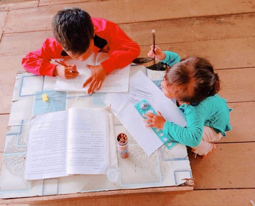 Side angle of a brother and sister sitting quietly together on a wooden floor doing their own work.