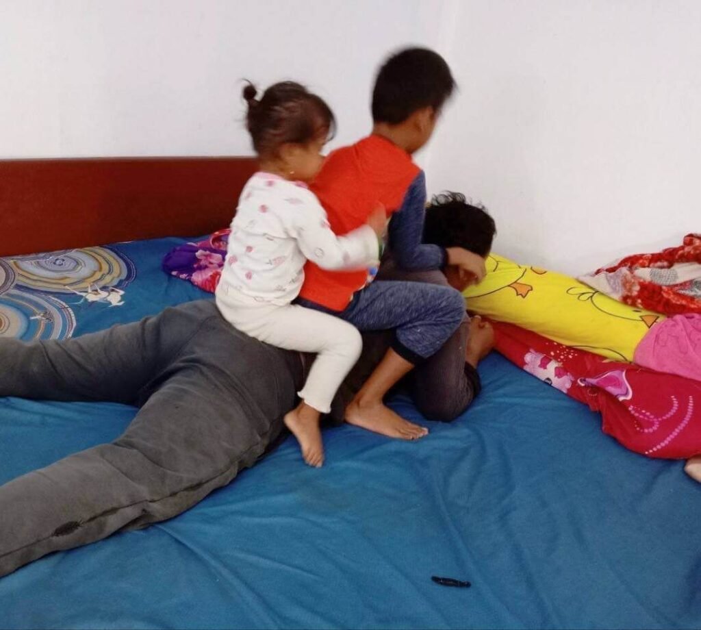 A boy and a younger girl playfully climbing on their father's back on a bed, participating in a game called "Motorbike."