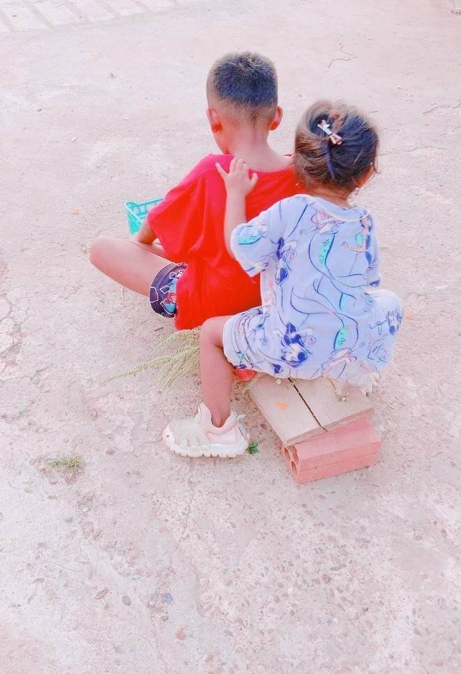A young boy and his toddler sister sitting together on a wooden plank, pretending to ride a motorcycle or bicycle.