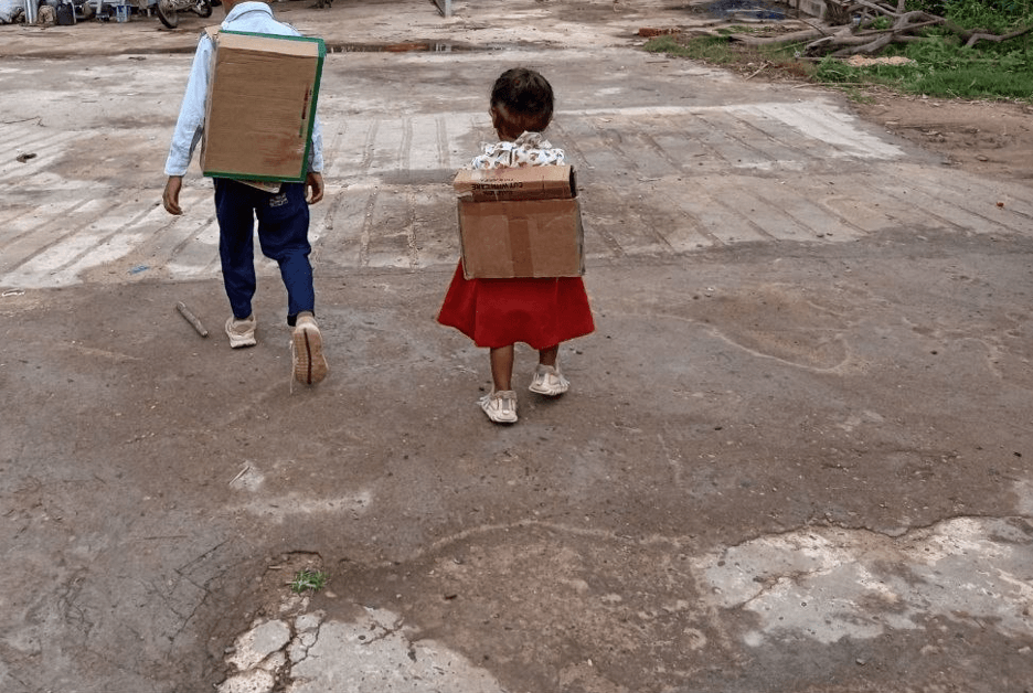 A brother and sister walking away from the camera, wearing their DIY cardboard box backpacks.
