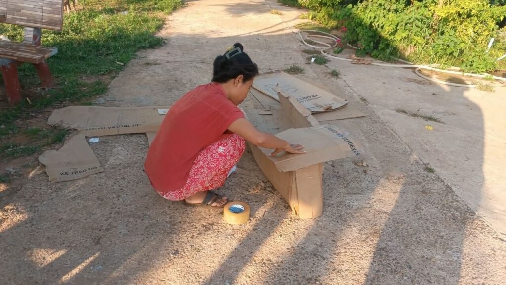 A person using packing tape outside to secure the folded front flaps of a cardboard boat.