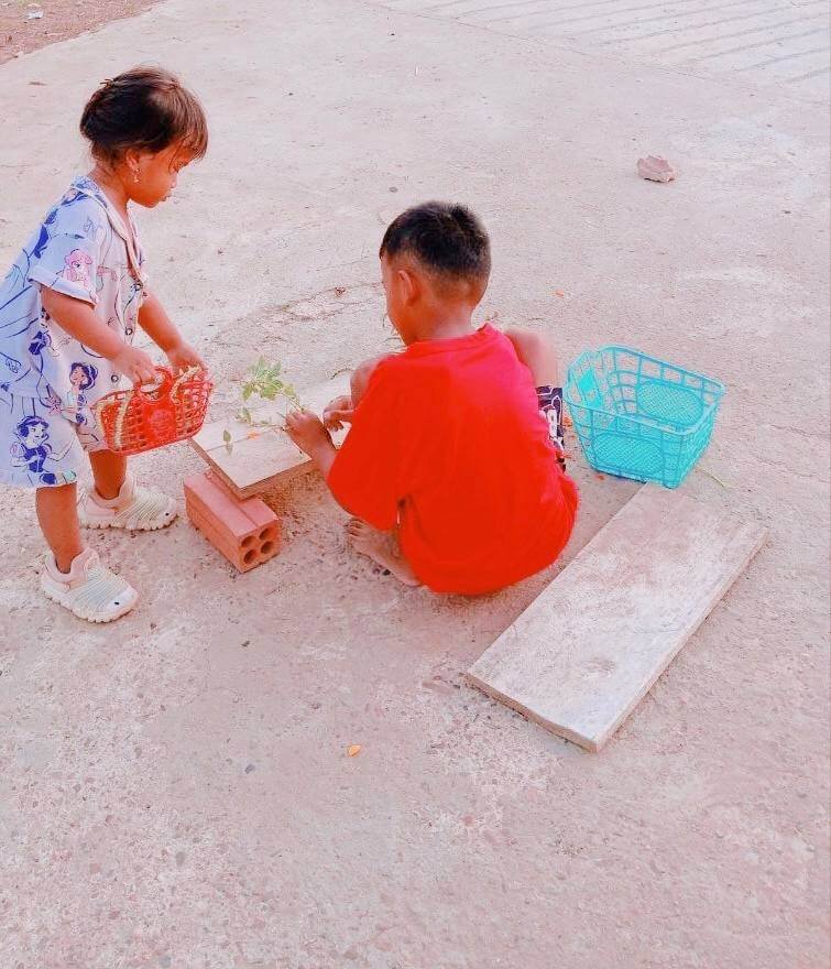 A toddler girl holding a small red basket while shopping for green leaves at her older brother's backyard market.