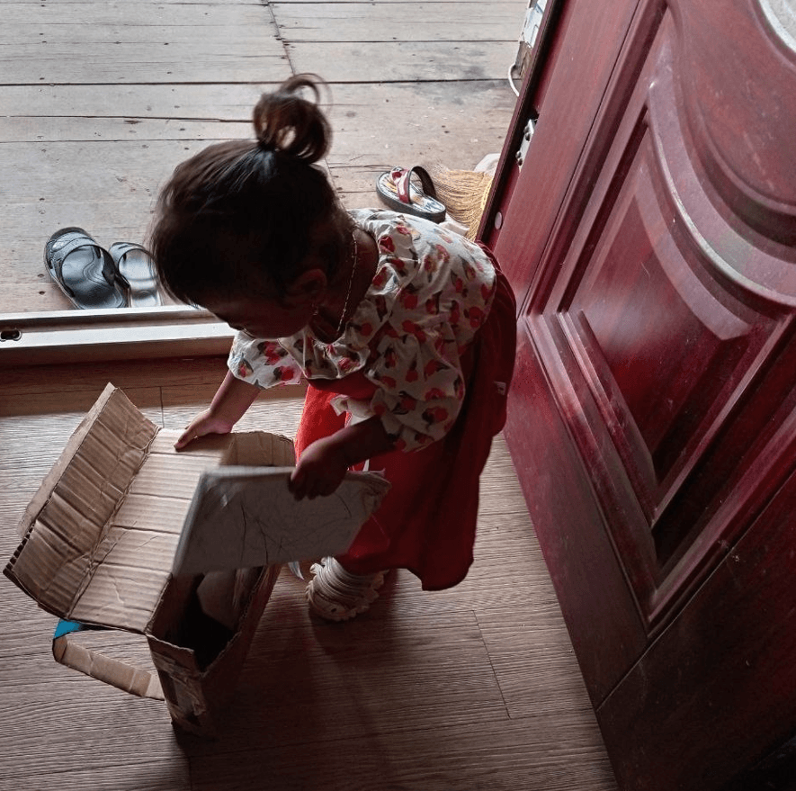 A toddler girl putting a book inside her new DIY cardboard backpack.
