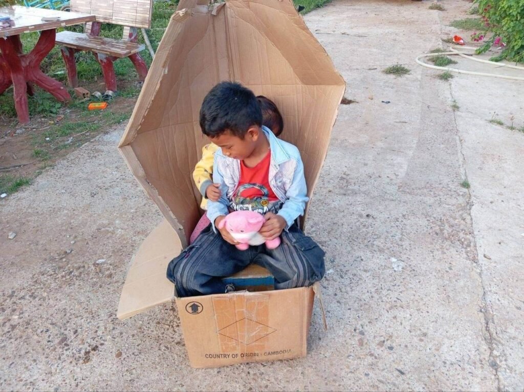 A brother and sister sitting squeezed together inside a small homemade cardboard box car.