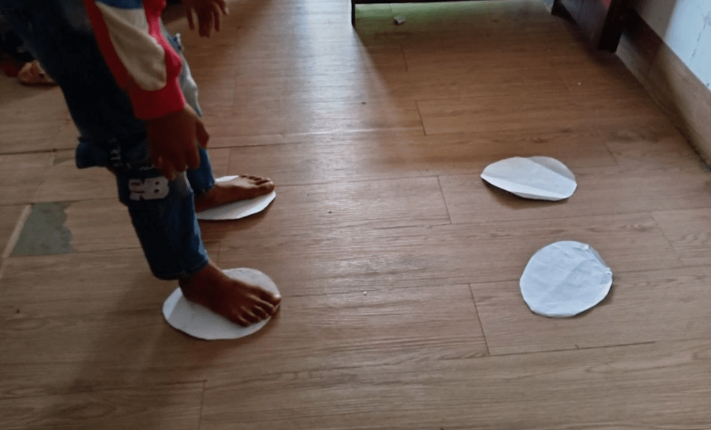 A child stepping on white paper circles on a wooden floor to avoid touching the ground.
